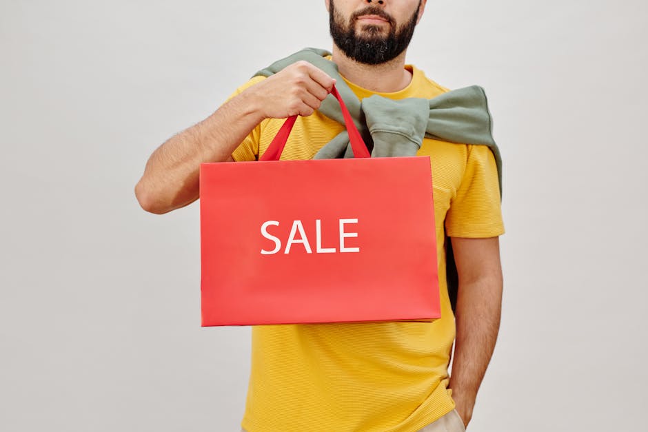 Person in yellow shirt holding a red sale shopping bag against white background.