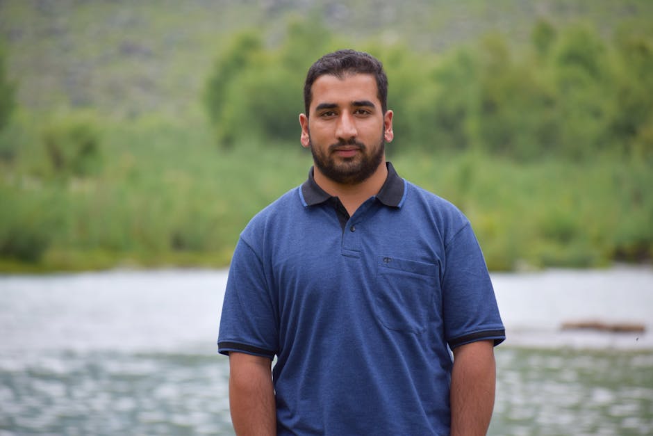 Portrait of a man with a beard wearing a polo shirt near a serene lake.