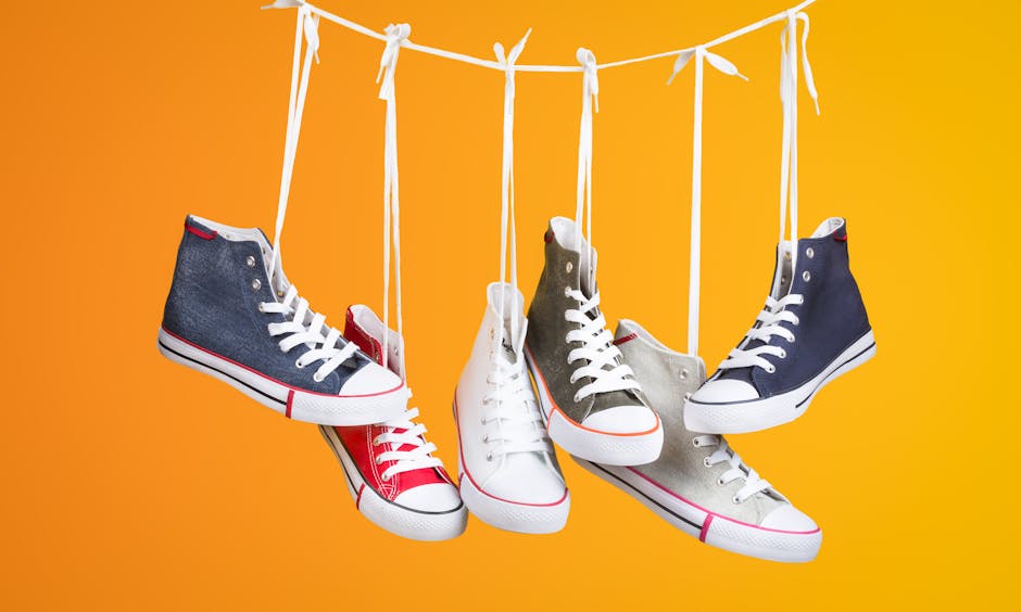 Stylish sneakers in various colors hanging with laces on a vivid orange backdrop. Ideal for fashion themes.