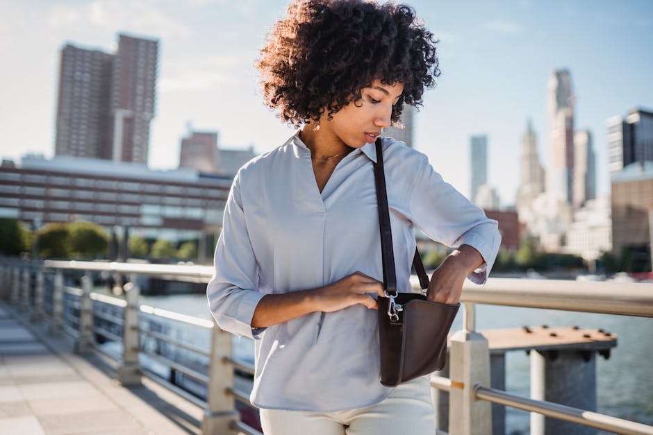 A black woman in an urban setting looks into her bag during the daytime. Bright and modern cityscape.