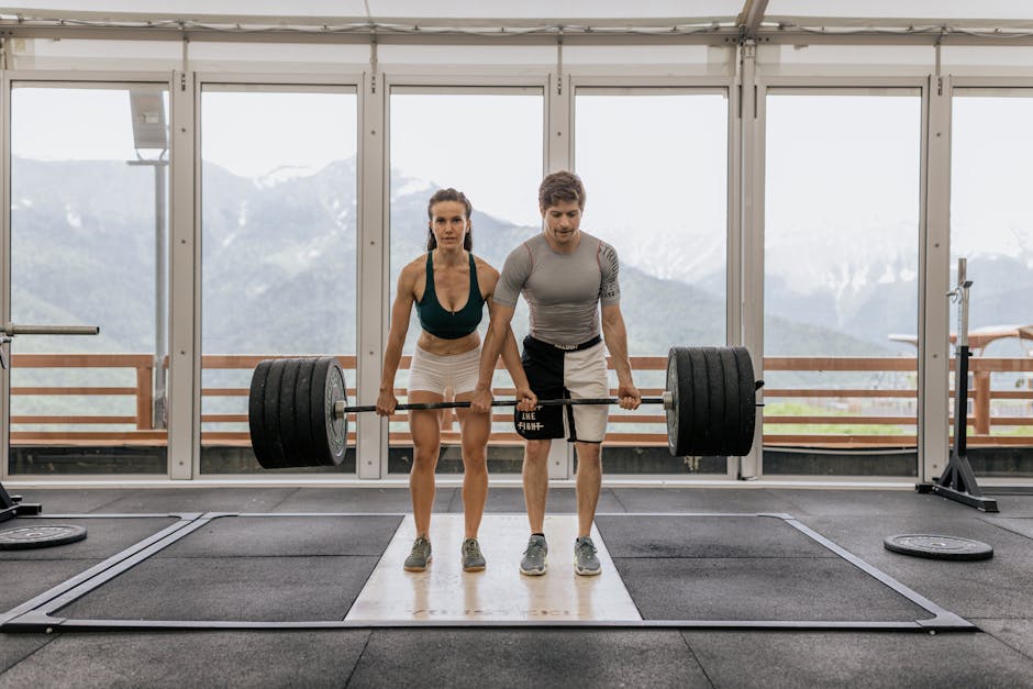 A couple engaged in weightlifting, showcasing strength and fitness in an indoor gym with a scenic mountain view.