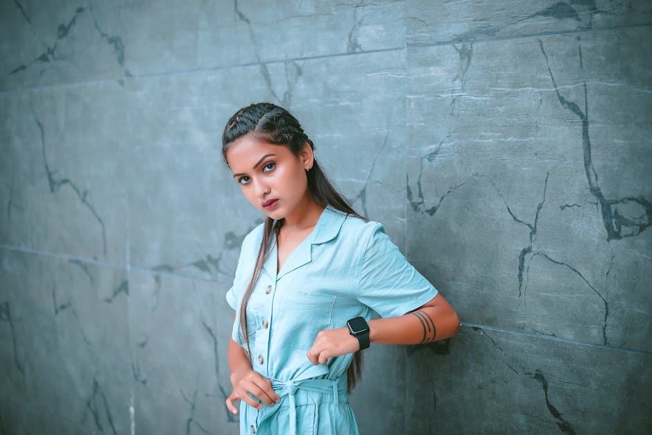 Portrait of a young woman with braided hair standing against a textured concrete wall.